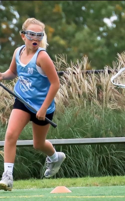 A girl is running with her lacrosse stick.