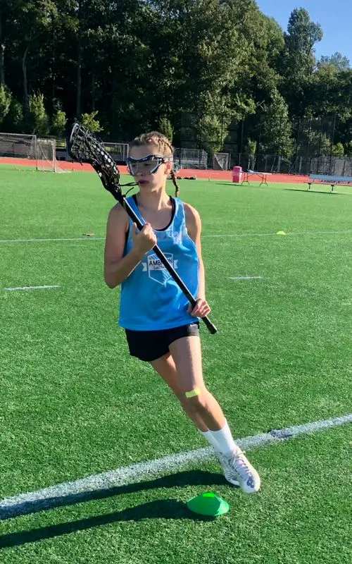 A girl is running on the field with her lacrosse stick.