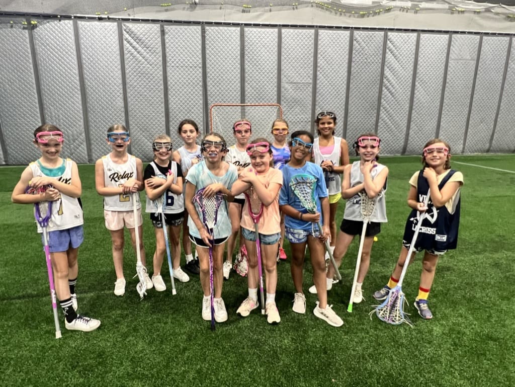 A group of young girls standing in the grass holding lacrosse sticks.