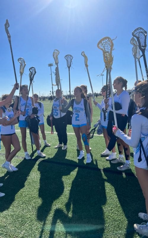 A group of girls holding lacrosse sticks on top of a field.