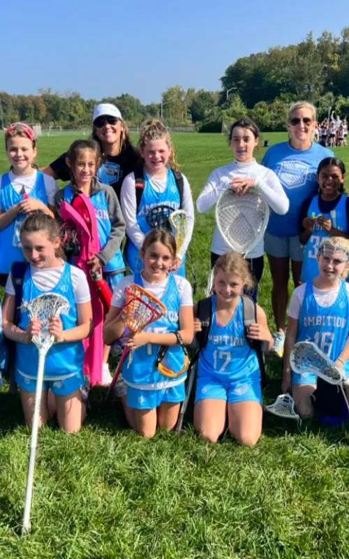 A group of girls in blue jerseys holding lacrosse equipment.