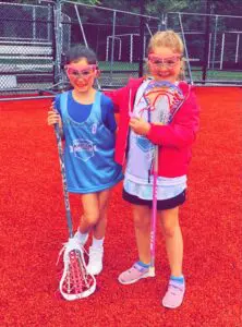 Two girls are posing for a picture while holding lacrosse sticks.