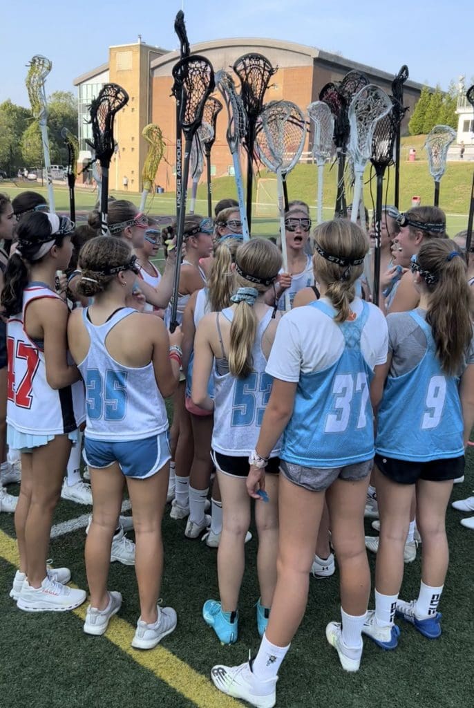 A group of girls standing around each other holding lacrosse sticks.