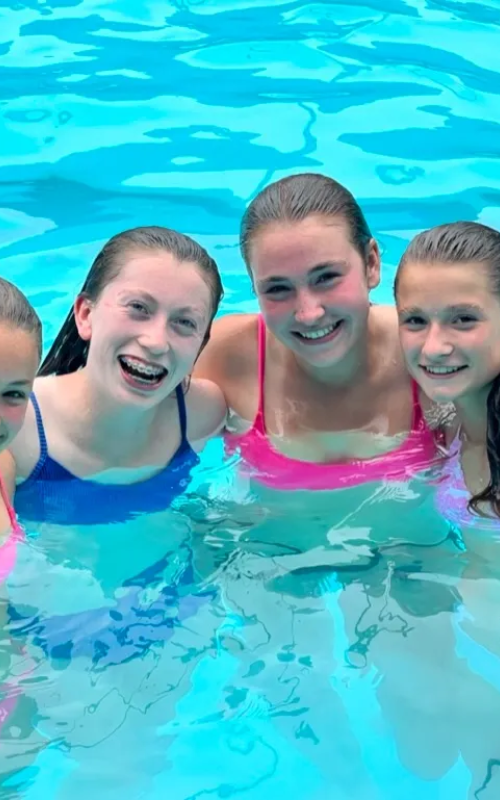 A group of girls in the pool smiling for the camera.