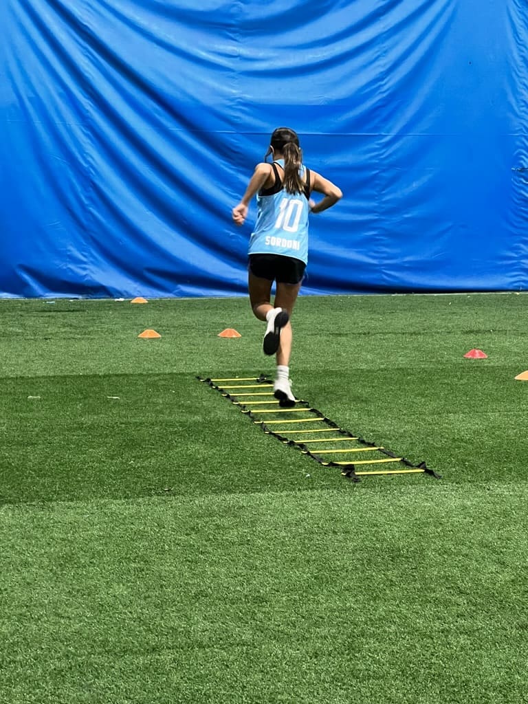 A person running on grass with agility ladders.