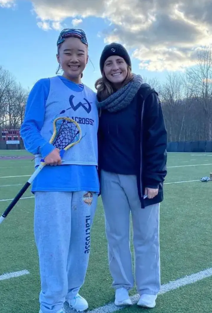 Two women standing on a field with lacrosse sticks.