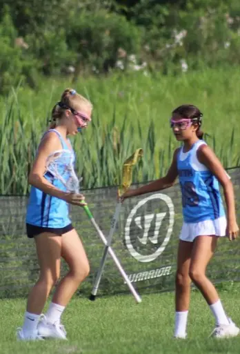Two girls are playing lacrosse on a field.