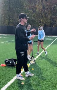 Lacrosse coach instructing players on field.